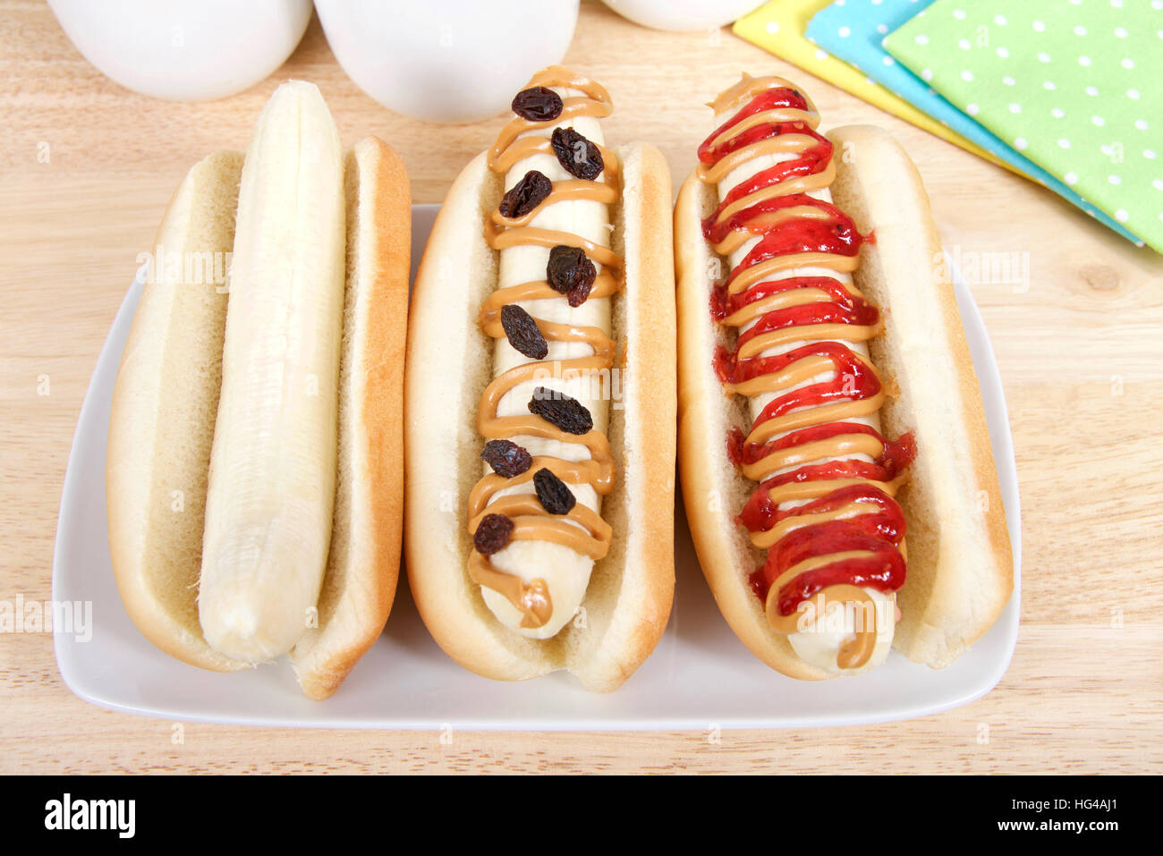 banana dog sandwiches on rectangular plate yellow, green and blue polka dot napkins cups behind in background. Banana in a hot dog bun, plain, with pe Stock Photo