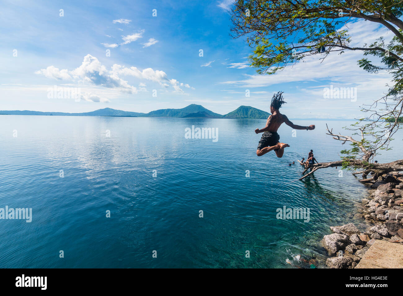 Man jumping in the bay of Rabaul with Volcano Tavurvur in the background, East New Britain, Papua New Guinea, Pacific Stock Photo