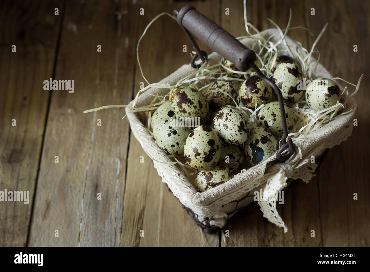 Quail eggs in a lined wire basket, on straw, on barn wood background, Easter, rustic vintage style, kinfolk, minimalistic Stock Photo