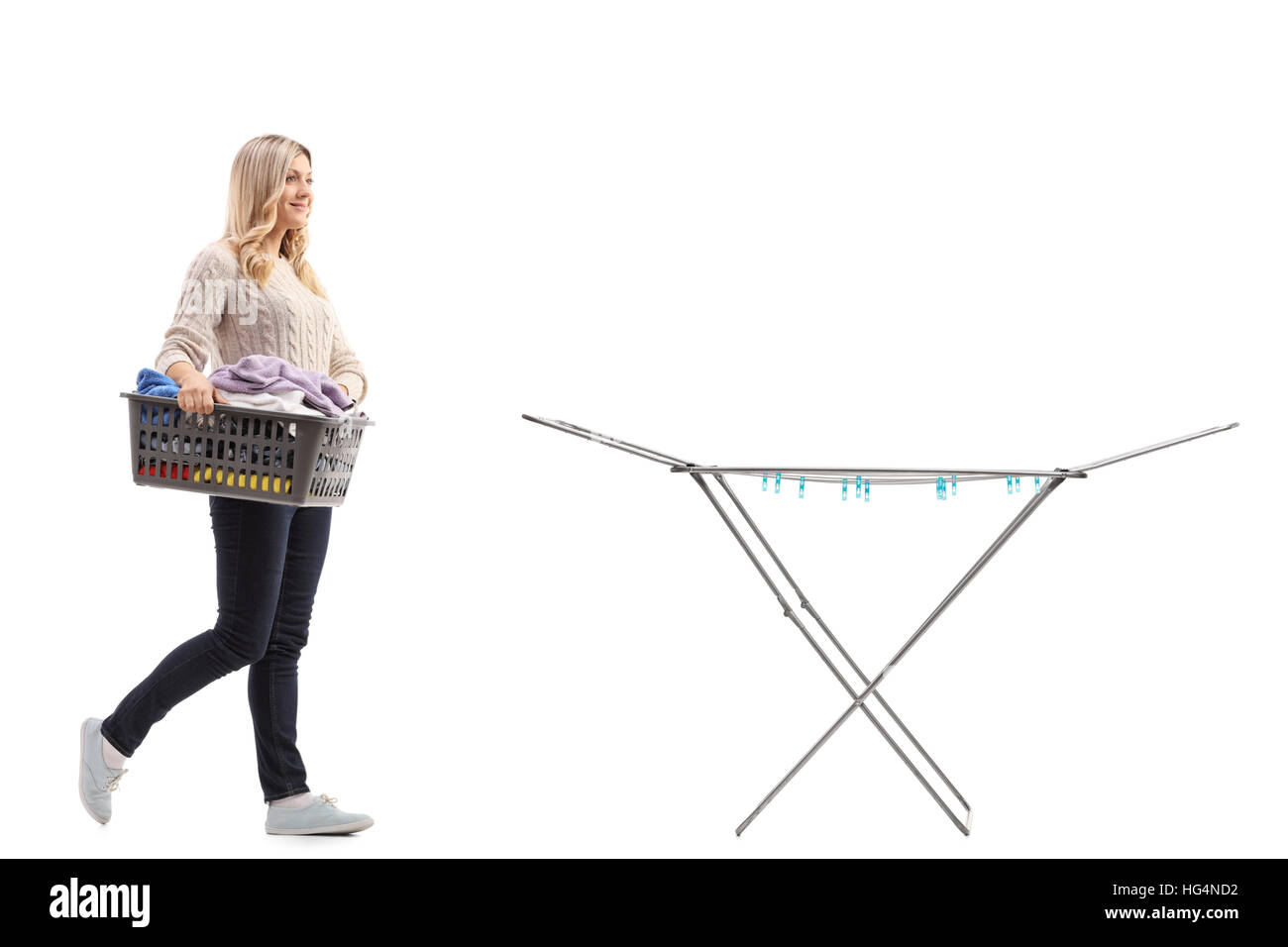 Full length portrait of a woman holding a laundry basket full of clothes and walking towards a clothing rack dryer isolated on white background Stock Photo