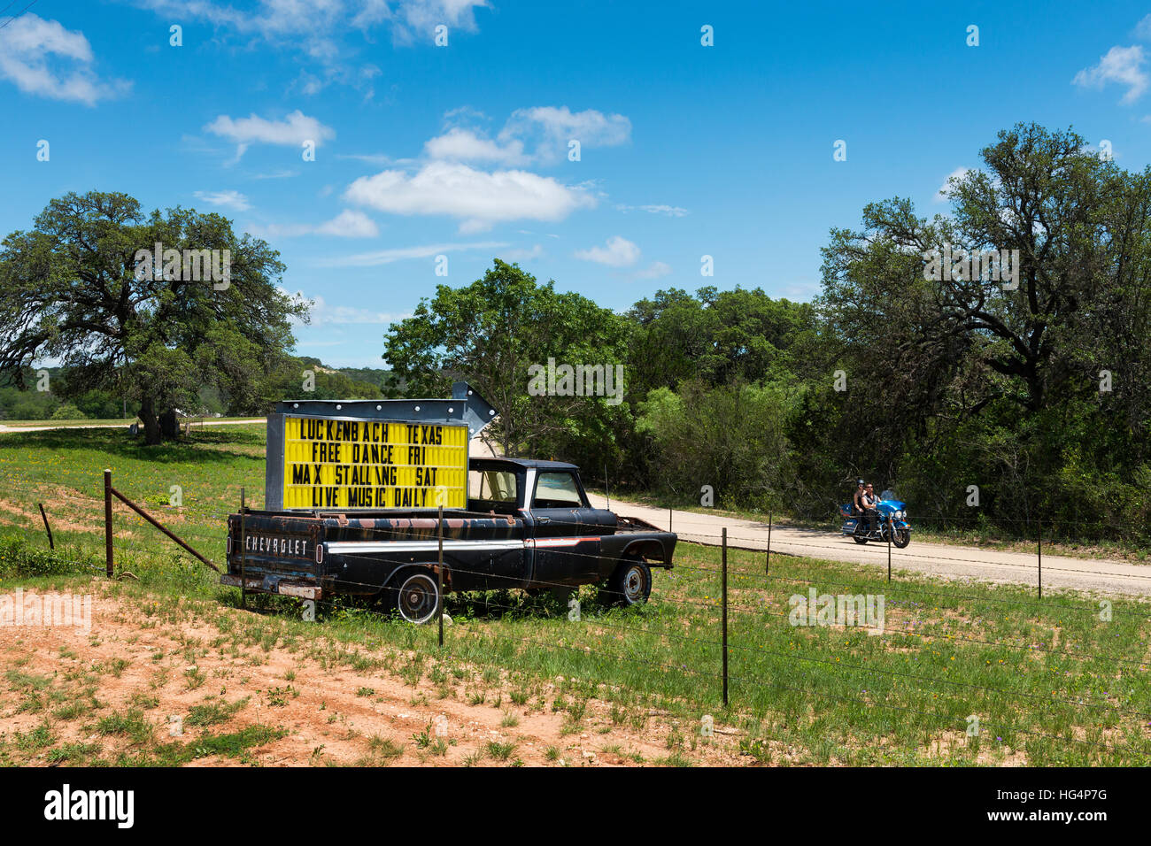 Luckenbach, Texas, USA - June 8, 2014: Couple in a motorbike passing by a truck with a sign for a music event in Luckenback, Texas. Stock Photo
