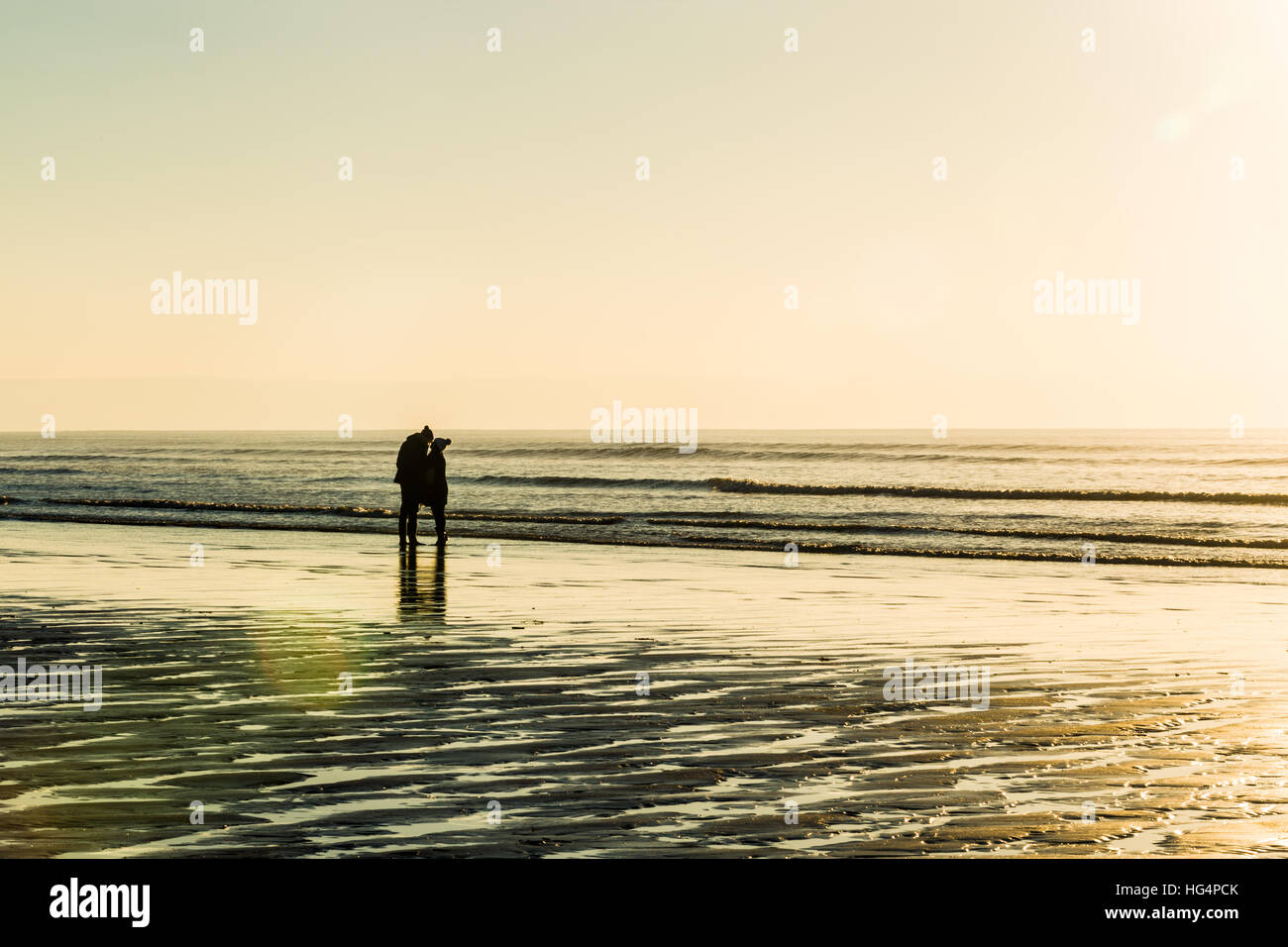 A young couple in love holding hands on a beach at sunset. Stock Photo