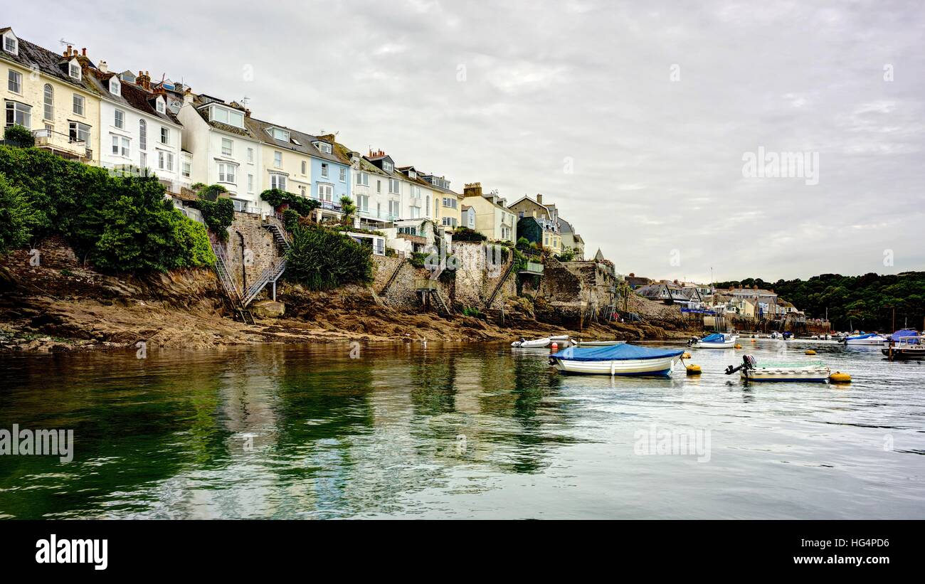 A panoramic landscape of moored boats in the Fowey Estuary looking up from the calm harbor water to the houses along the bank. Stock Photo