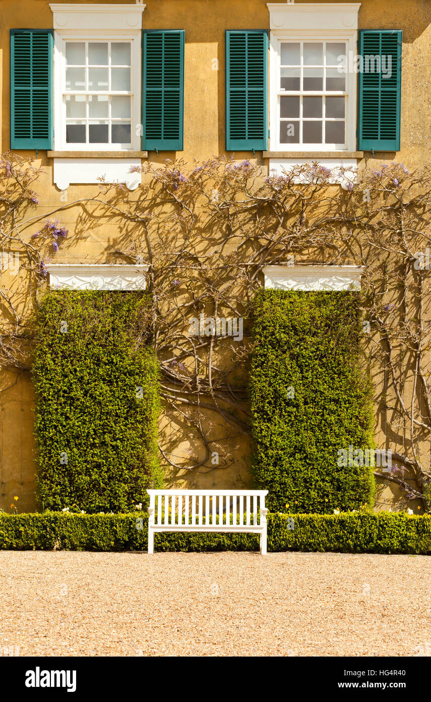 White wooden bench in front of old, golden stone house, with green ...