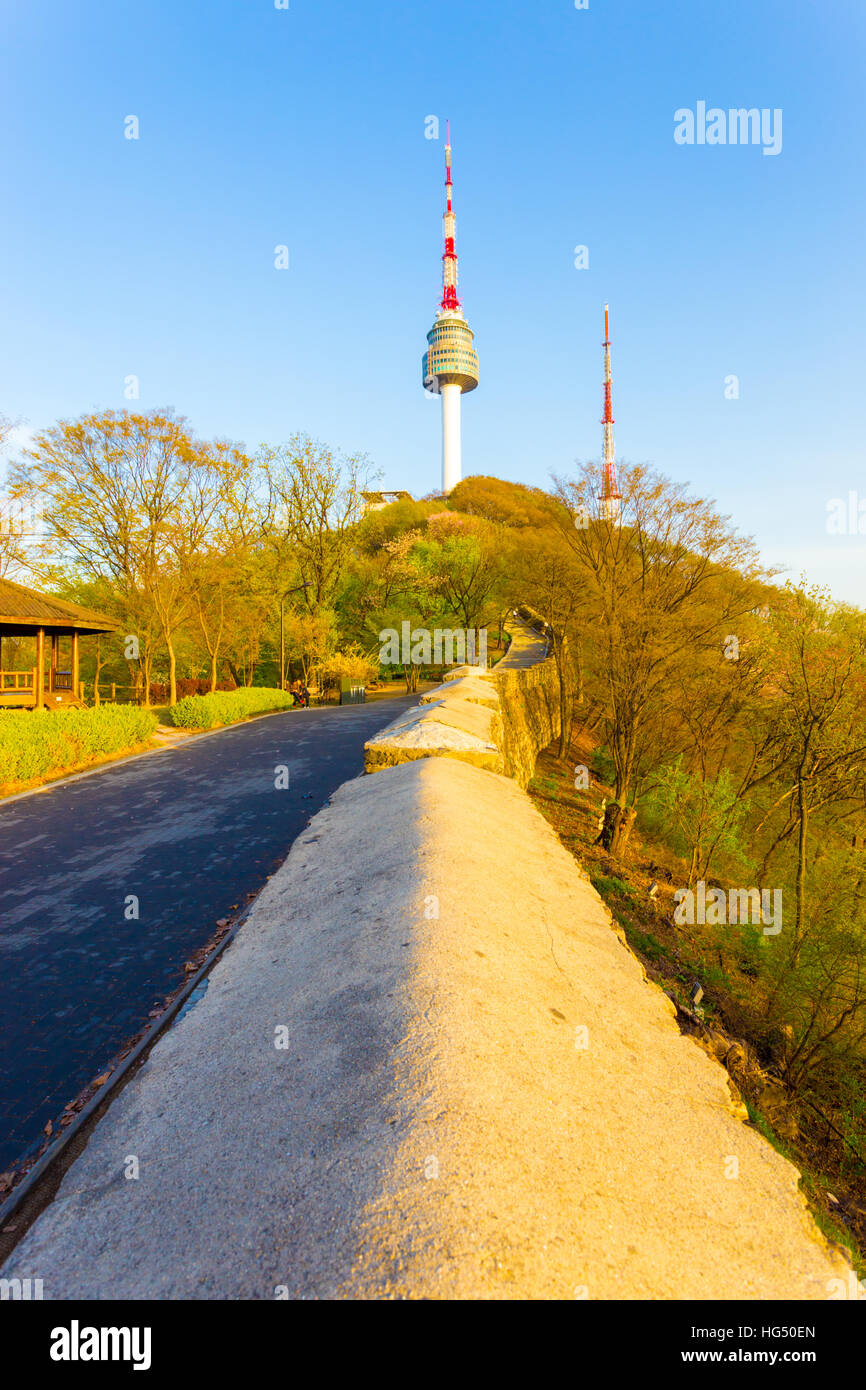 The old city wall leads to peak of Namsan mountain and the YTN Seoul Tower on a clear, blue sky evening in South Korea Stock Photo