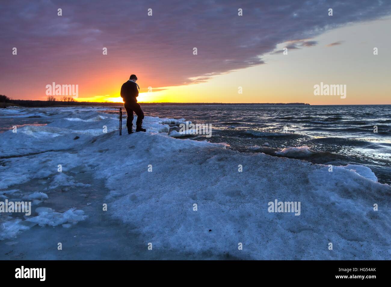 Winter Photography . Male photographer standing in the snow on the shore of a frozen lake with a sunset hoirizon. Port Austin, M Stock Photo