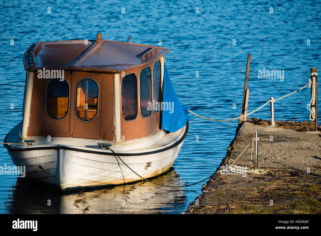 Houseboat or up cycled fishing boat as seen from the aft. Boat is tied to a pier in calm water. Stock Photo