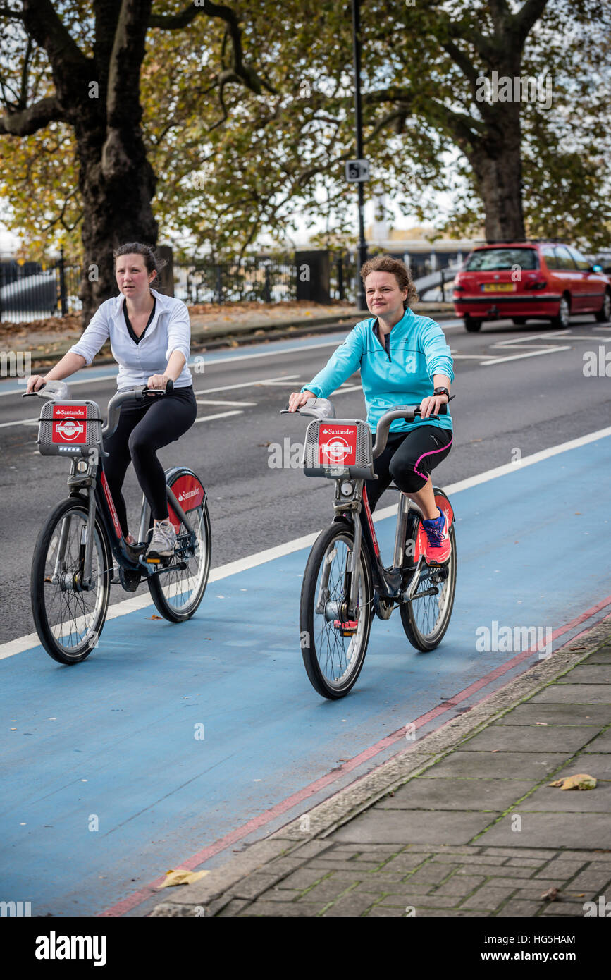 Mid 20s-30s women riding self-hire bicycles in London to help combat traffic congestion and climate change Stock Photo