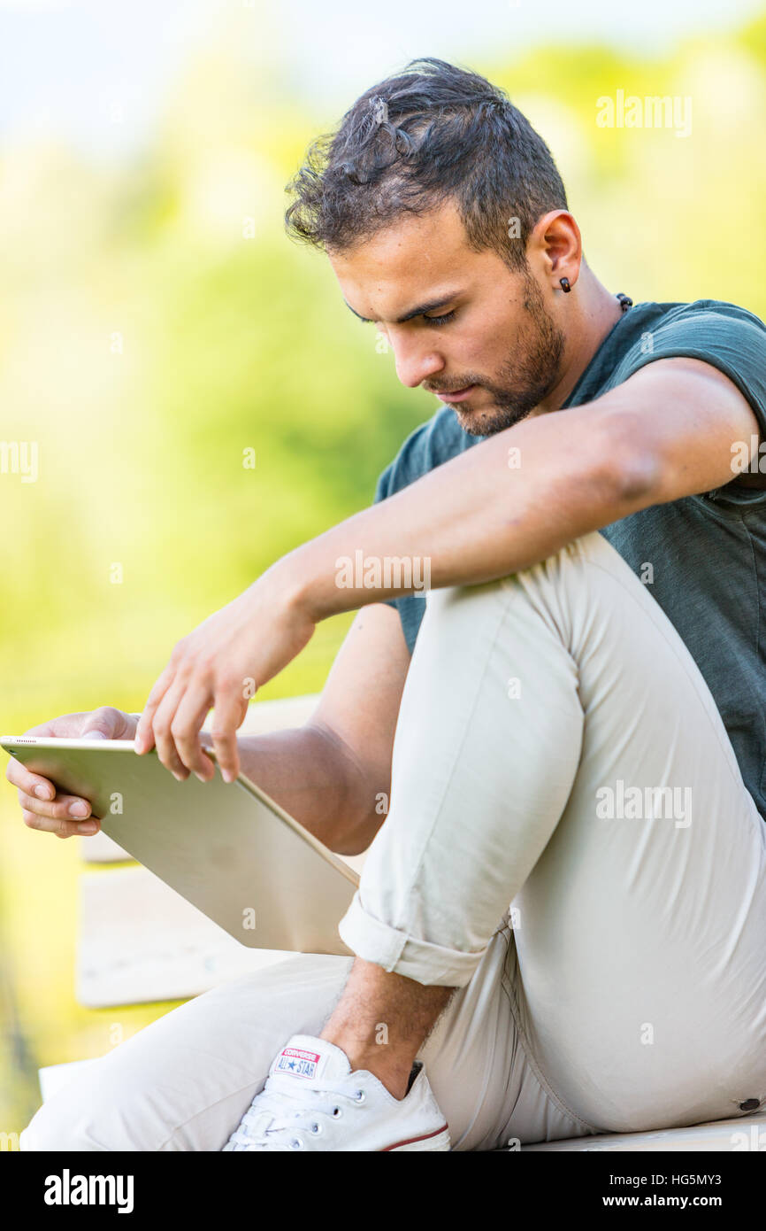 young handsome man working or enjoying his digital tablet outdoors Stock Photo