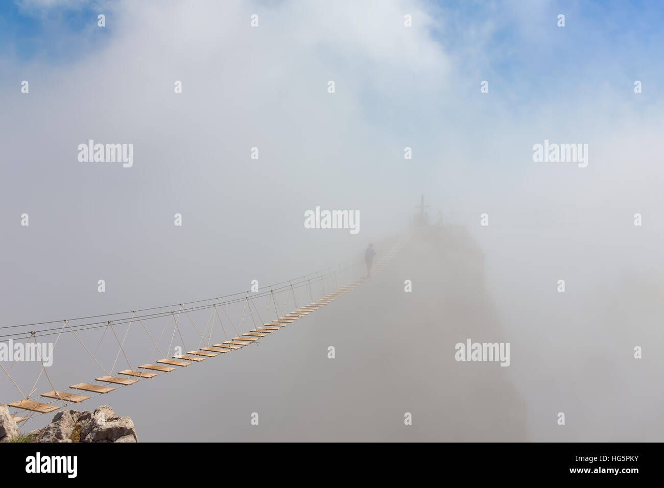 Man crossing the chasm on the hanging bridge in fog Stock Photo