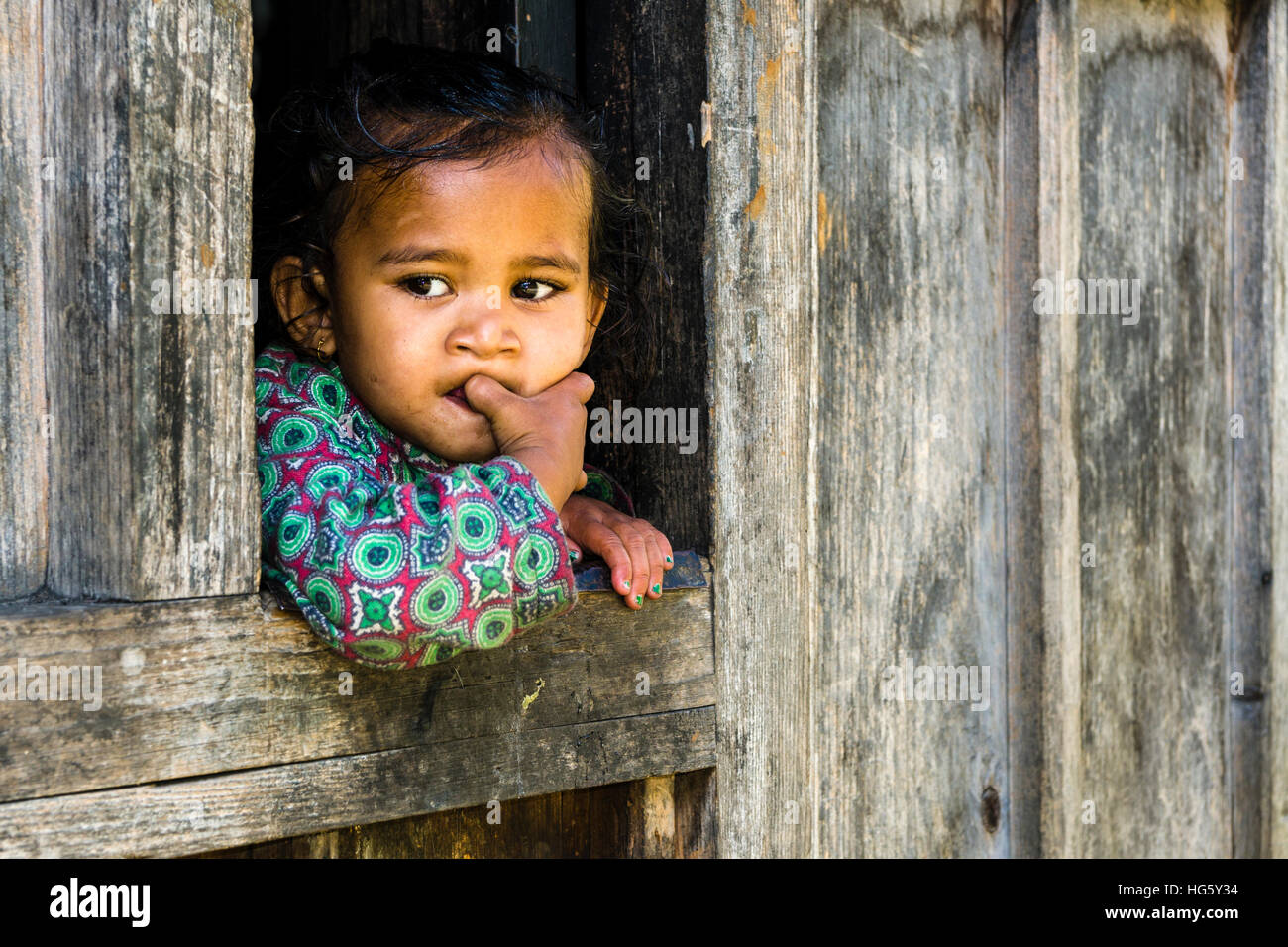 Portrait of a little girl, Upper Marsyangdi valley, looking out of a window, Bagarchap, Manang District, Nepal Stock Photo