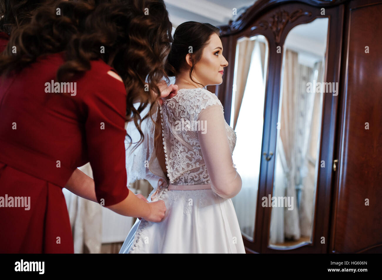 Two young and gorgeous bridesmaids on red dress wear bride on her room ...