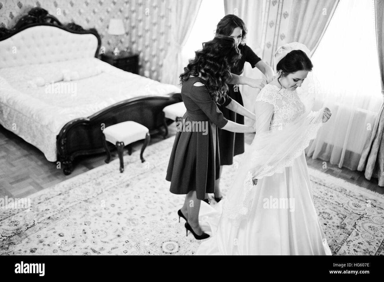 Two young and gorgeous bridesmaids on red dress wear bride on her room ...