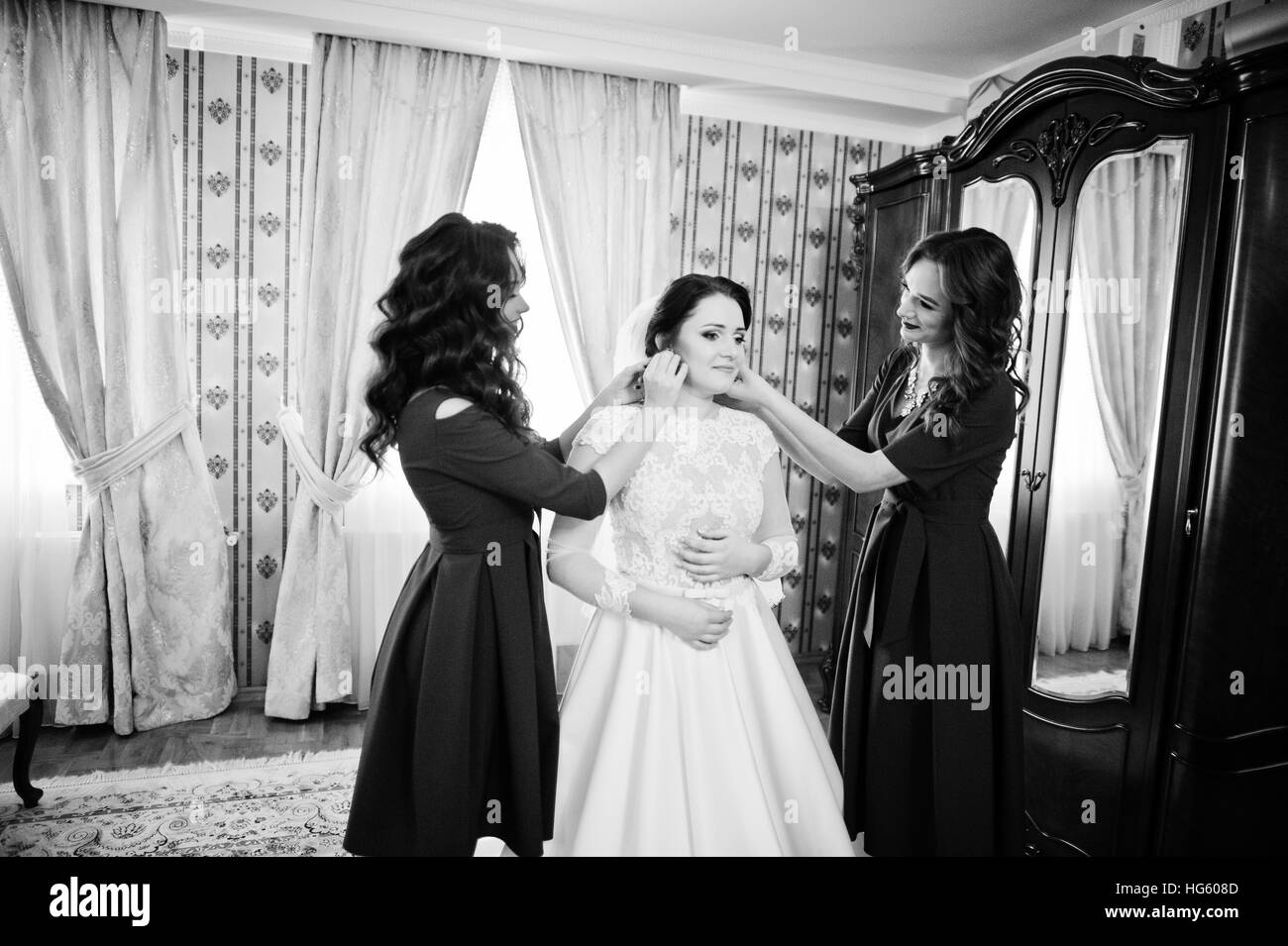 Two young and gorgeous bridesmaids on red dress wear bride on her room ...