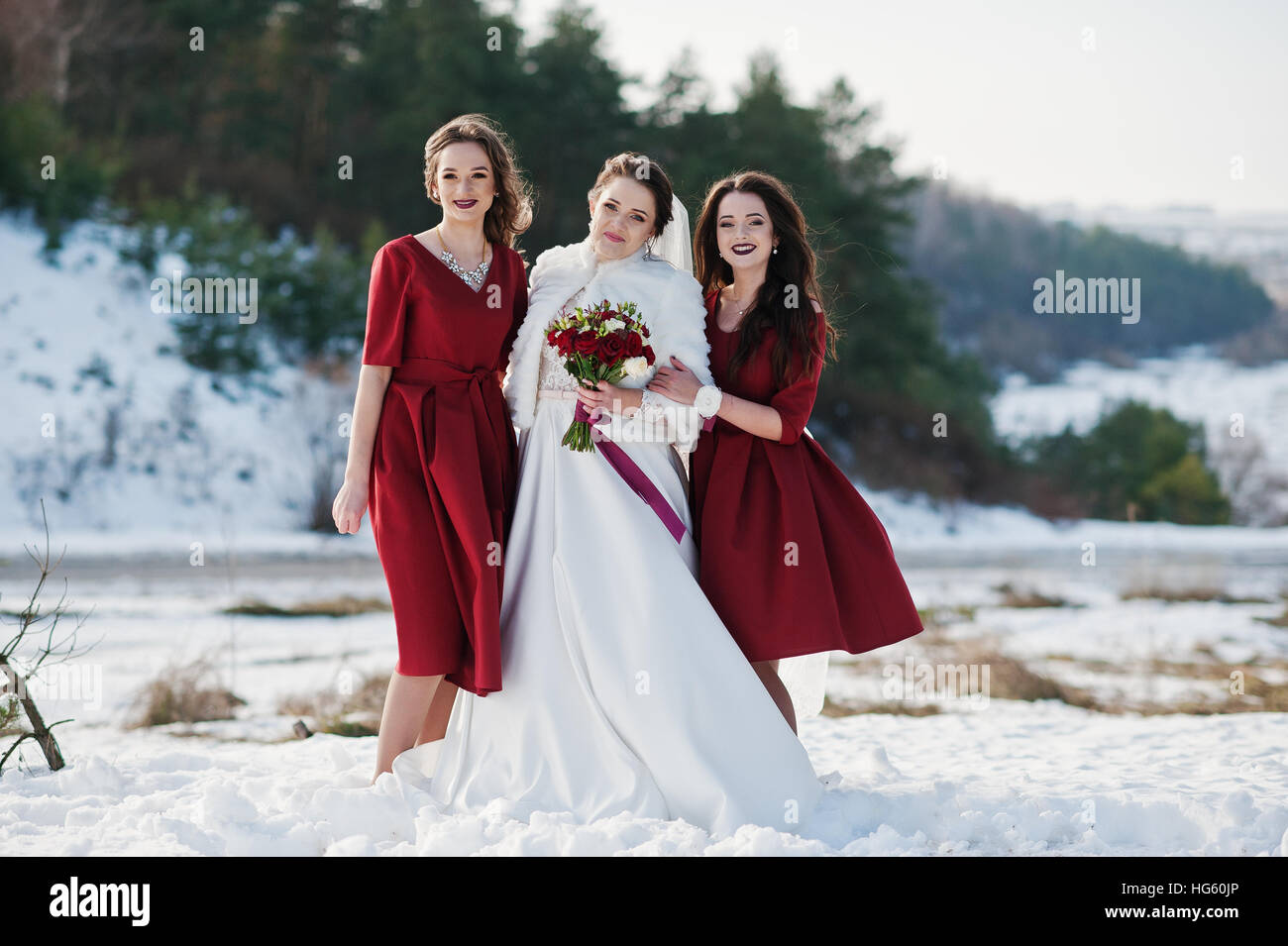 Pretty bridesmaids on red dresses with bride on sunny winter wedding day  Stock Photo