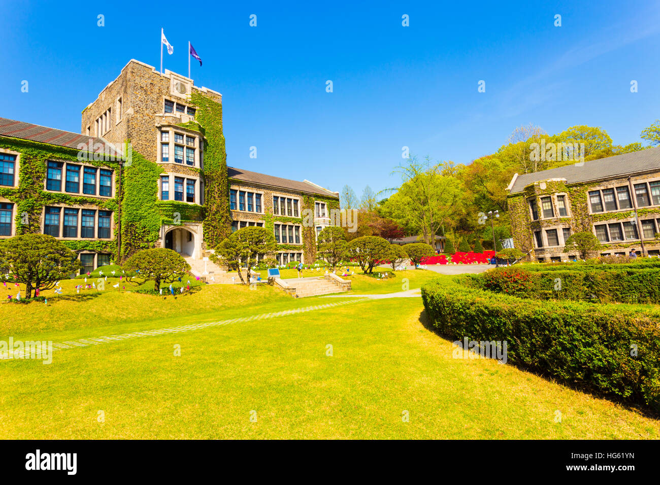 Flags flying over ivy covered main building above grassy quad at Yonsei University on a blue sky day in Sinchon, Seoul, Korea Stock Photo