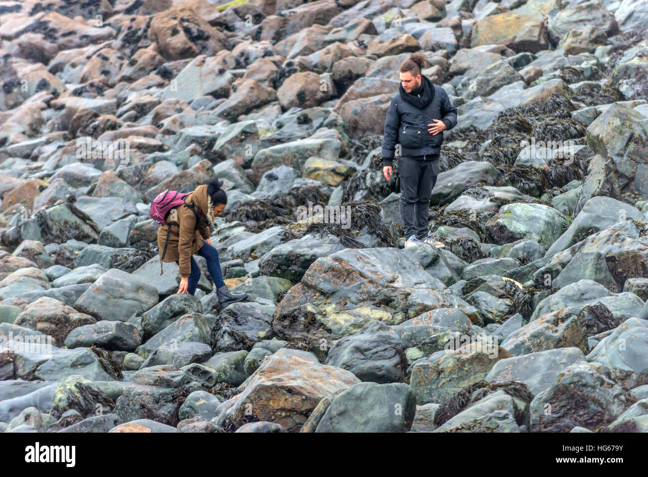 A young couple scramble over the rocks on the beach at St Ives in Cornwall Stock Photo