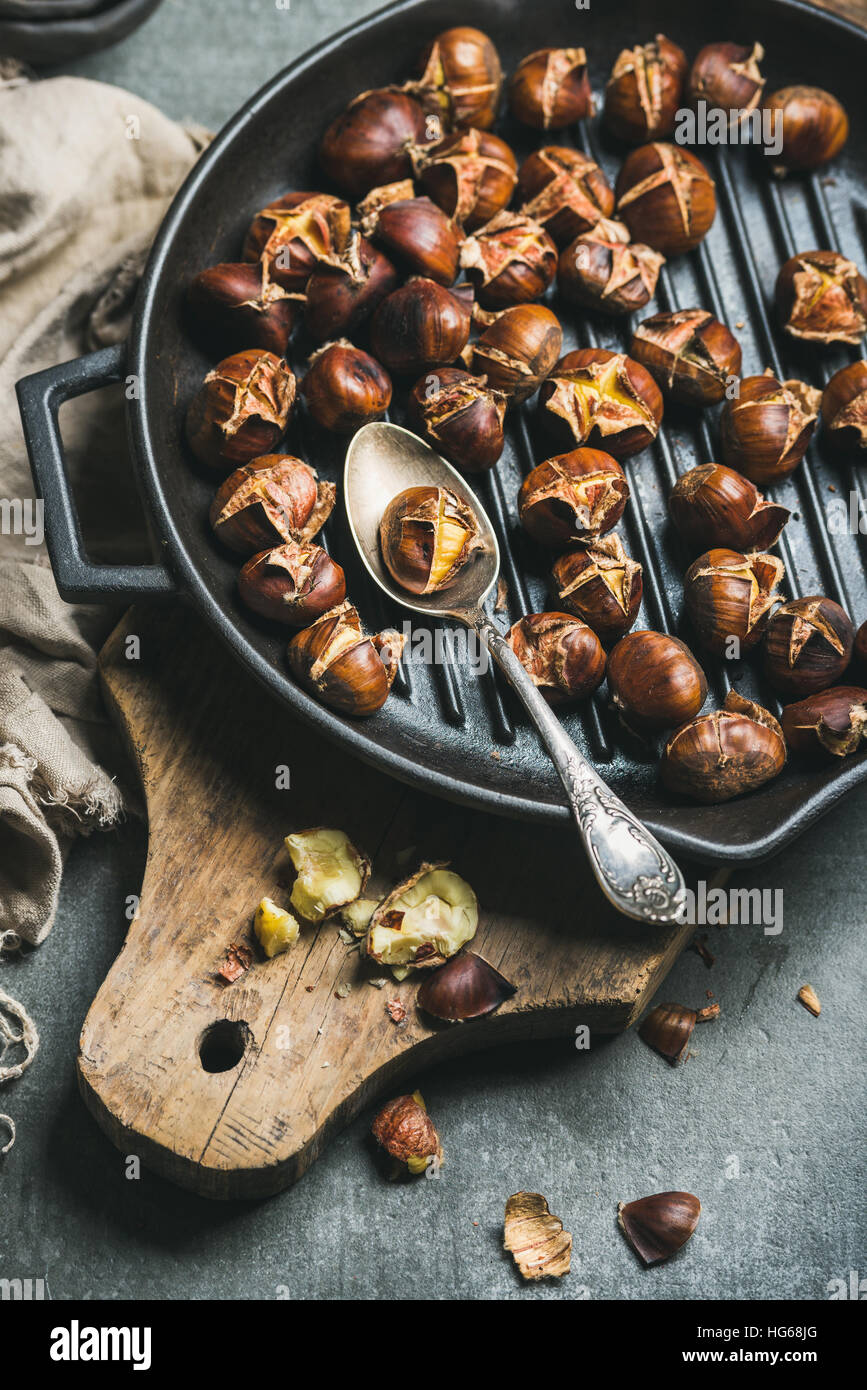 Roasted chestnuts in cast iron grilling pan over wooden board Stock