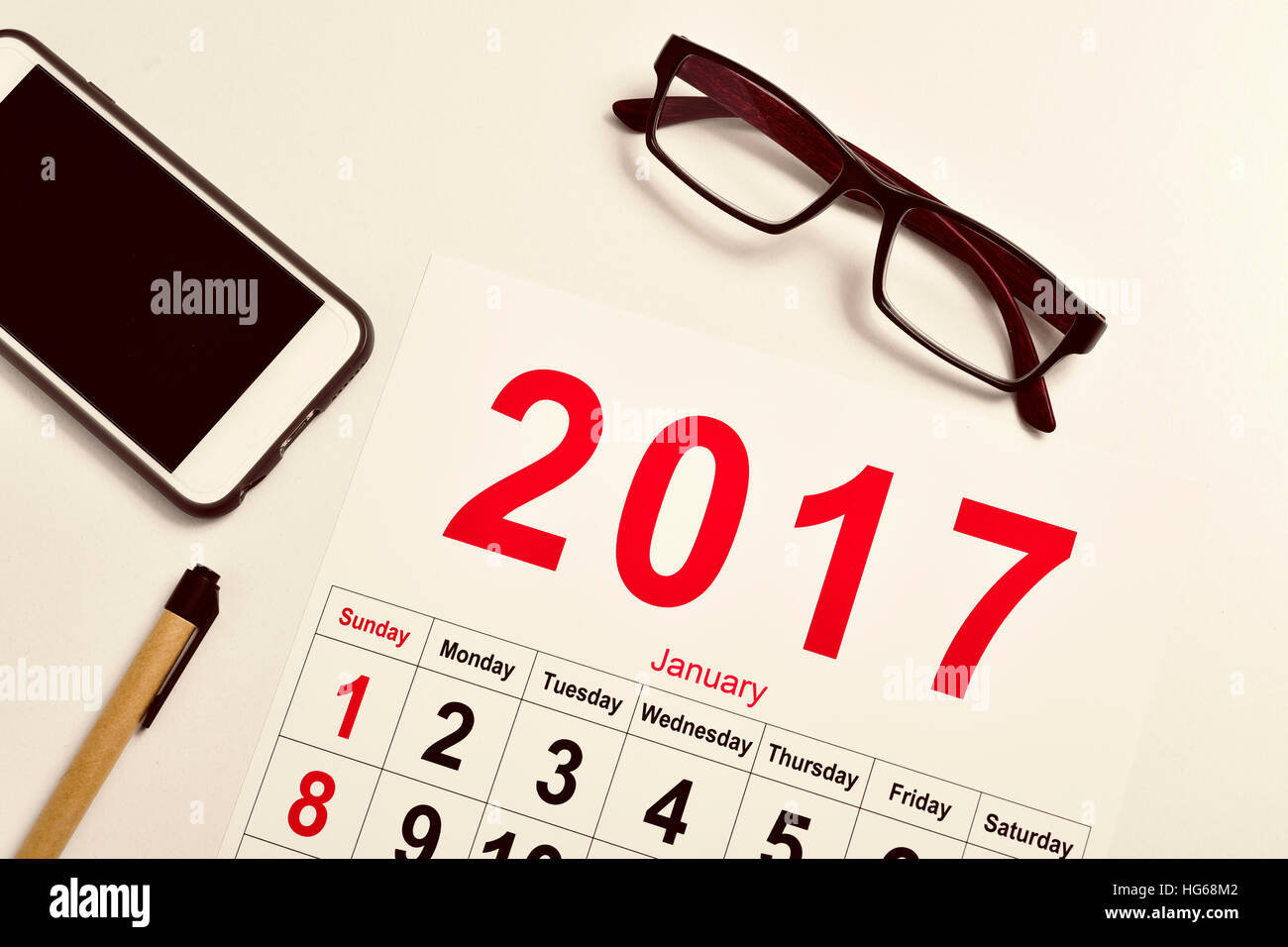 high-angle shot of a 2017 calendar, a pair of eyeglasses, a smartphone and a pen on a white office desk Stock Photo