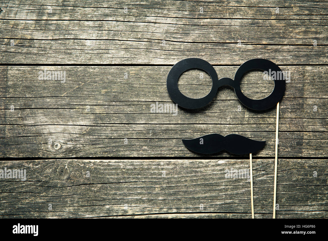 Fake glasses and mustaches on sticks on old wooden background. Stock Photo