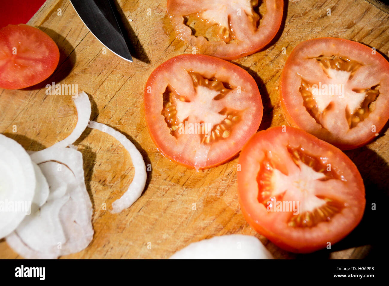 Photograph of a knife, tomato slices and onion on a wood cutting board Stock Photo
