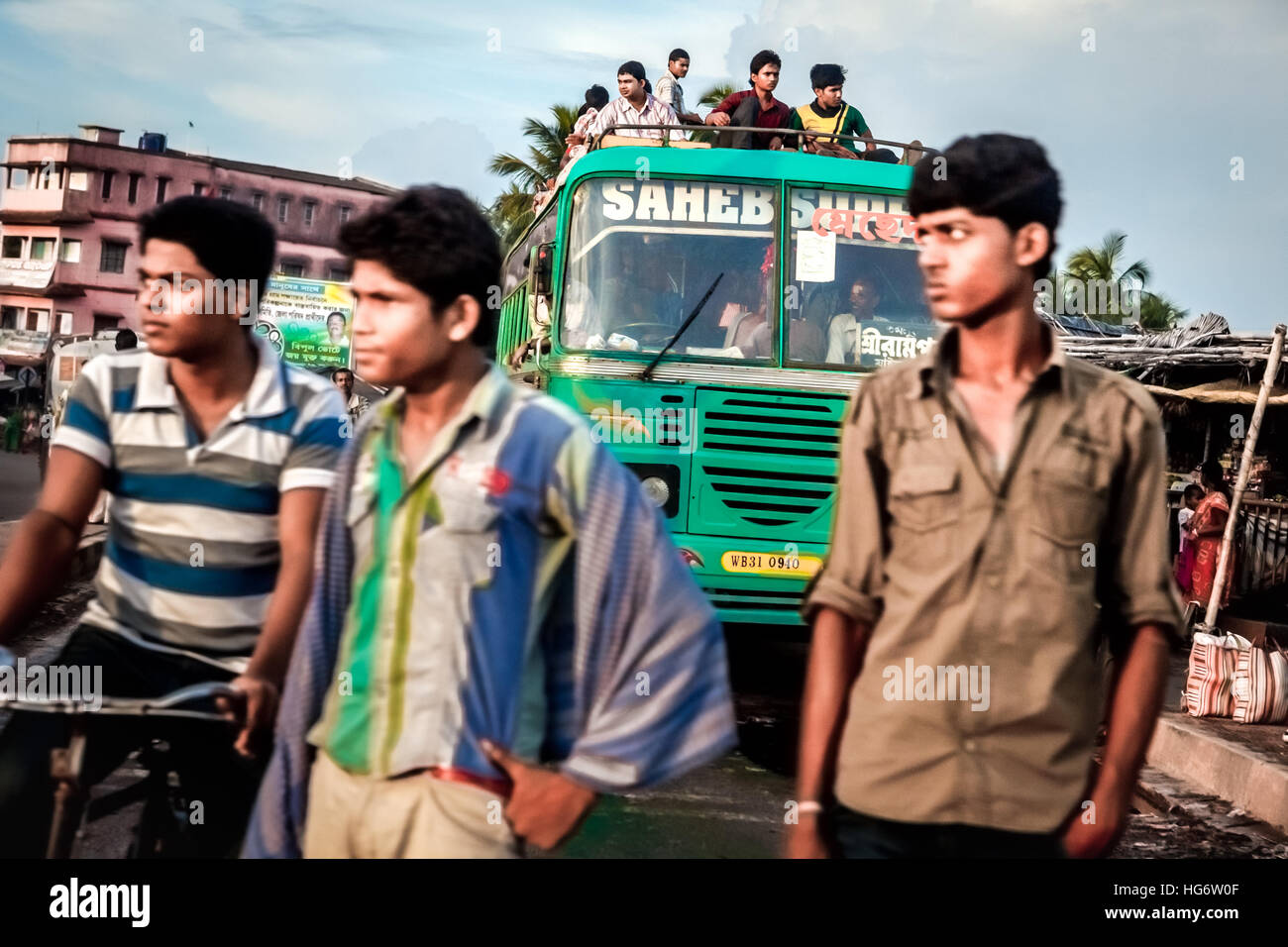Men waiting for a road crossing with a packed bus in the background, on a junction in Kolaghat, on the way to Haldia, West Bengal, India. Stock Photo