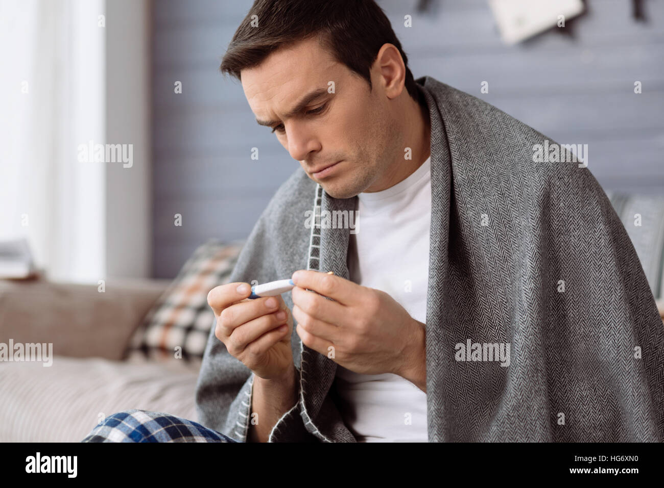 Unhappy ill man looking at the thermometer Stock Photo