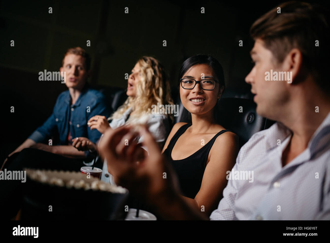 Happy young friends watching movie and talking in theater. Group of people in multiplex theater. Stock Photo