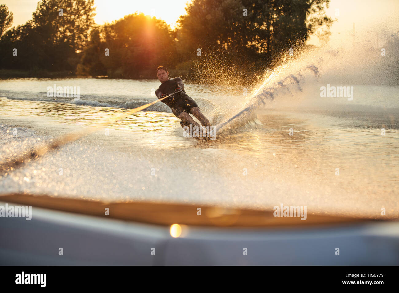 Man wakeboarding on lake behind boat. Water skiing on lake at sunset. Stock Photo