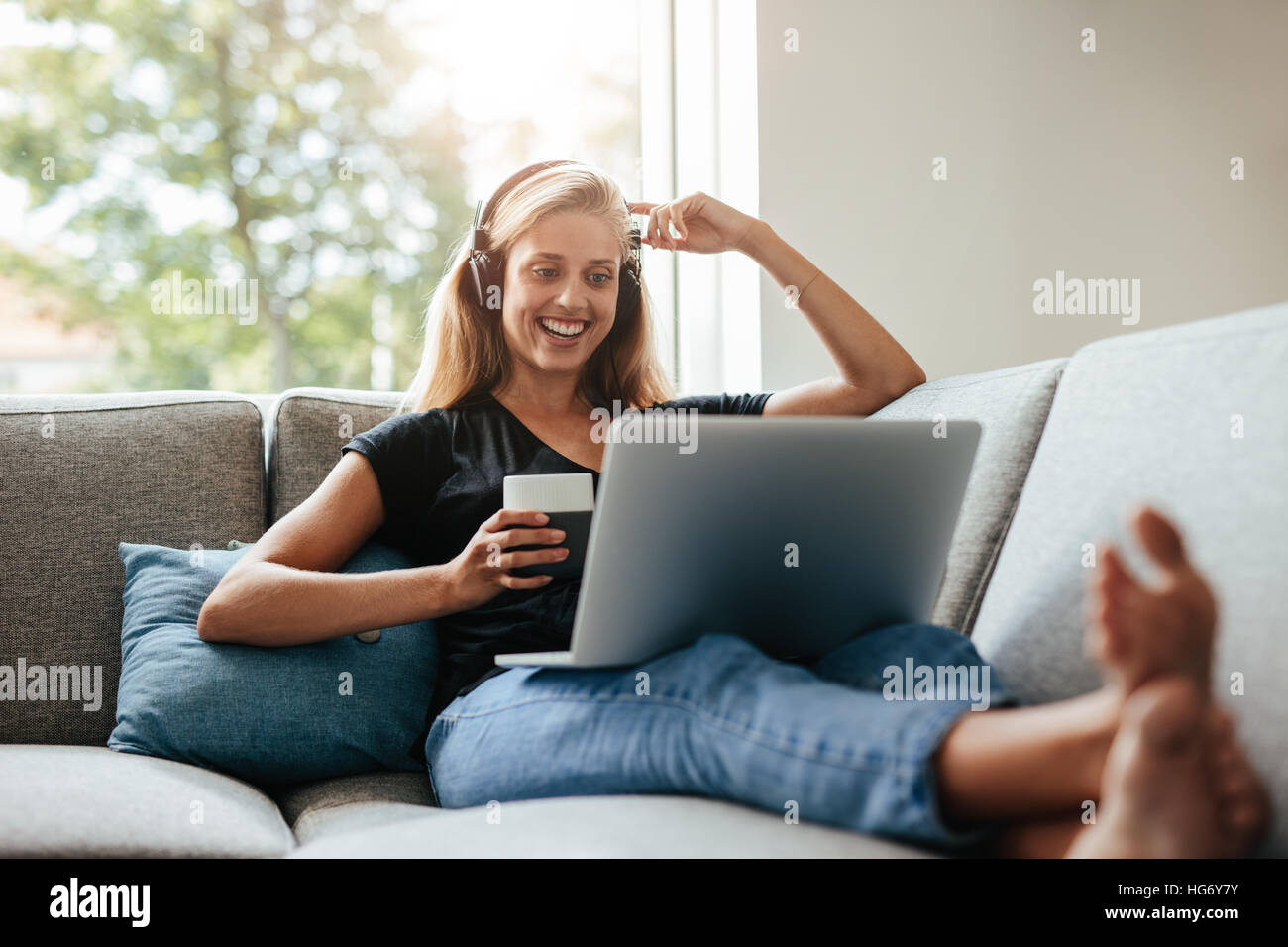 Smiling young woman enjoying a cup of coffee while relaxing with her ...
