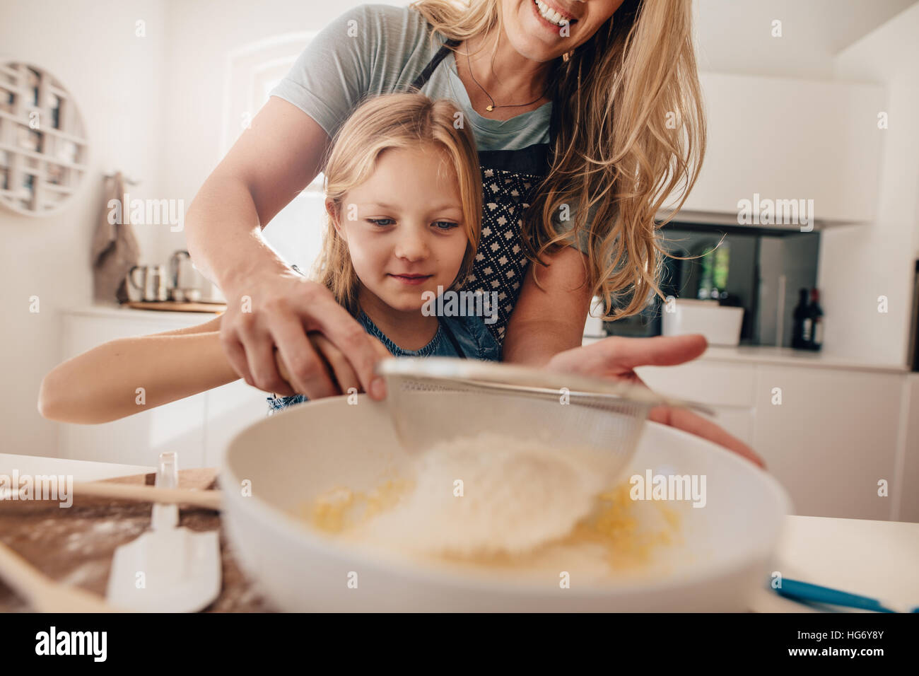Little girl learning to make batter from her mother. Woman adding flour in bowl. Mother and daughter making dough for baking. Stock Photo