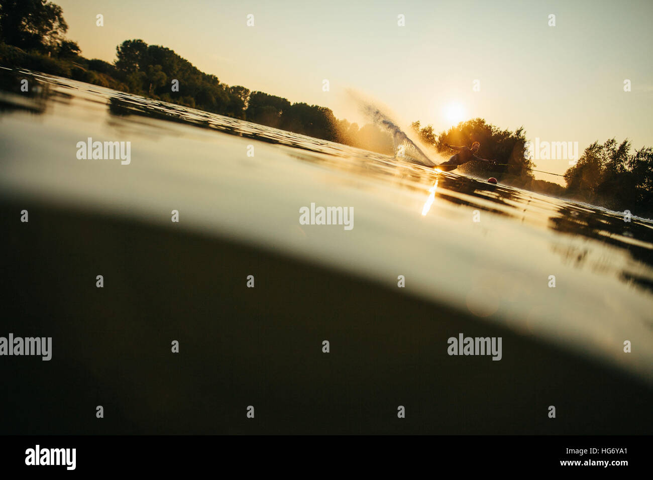 Low angle shot of man wakeboarding on a lake. Water skiing at sunset. Stock Photo