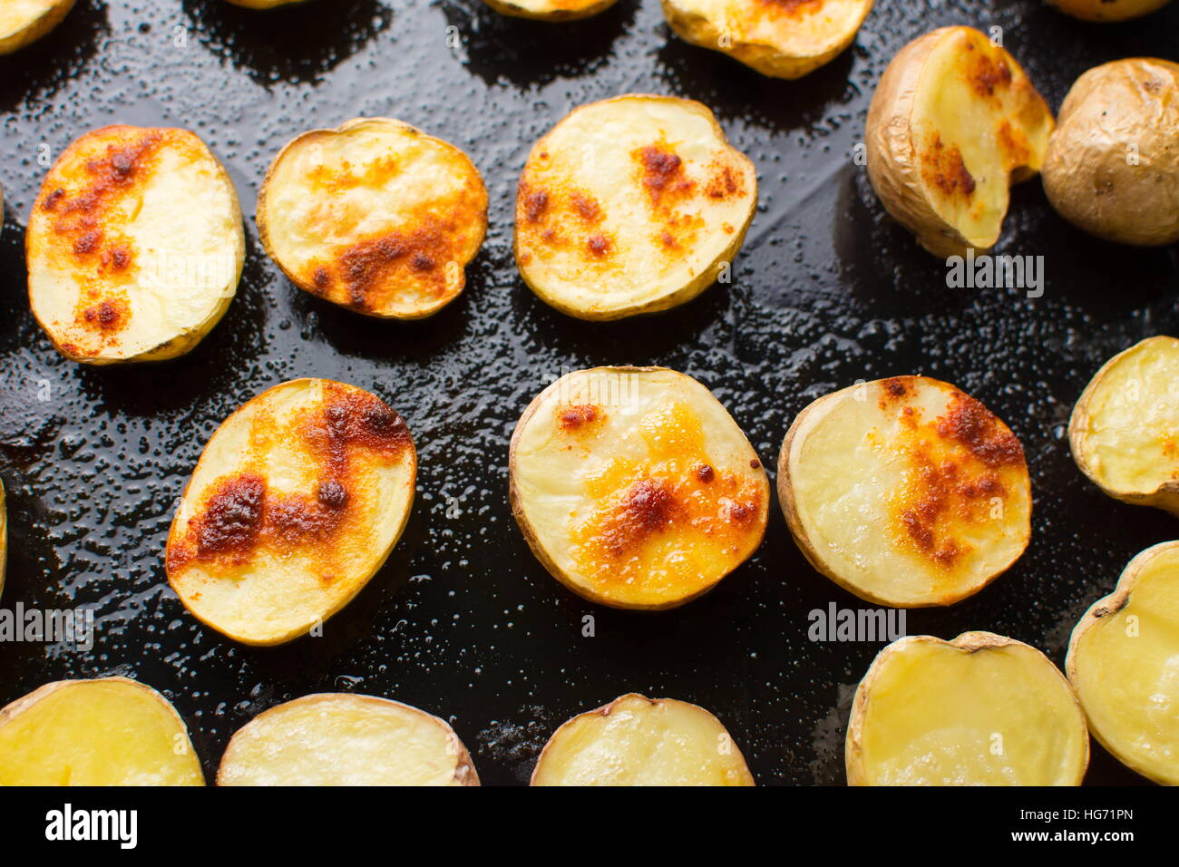 Roasted potato slices on a black baking plate Stock Photo