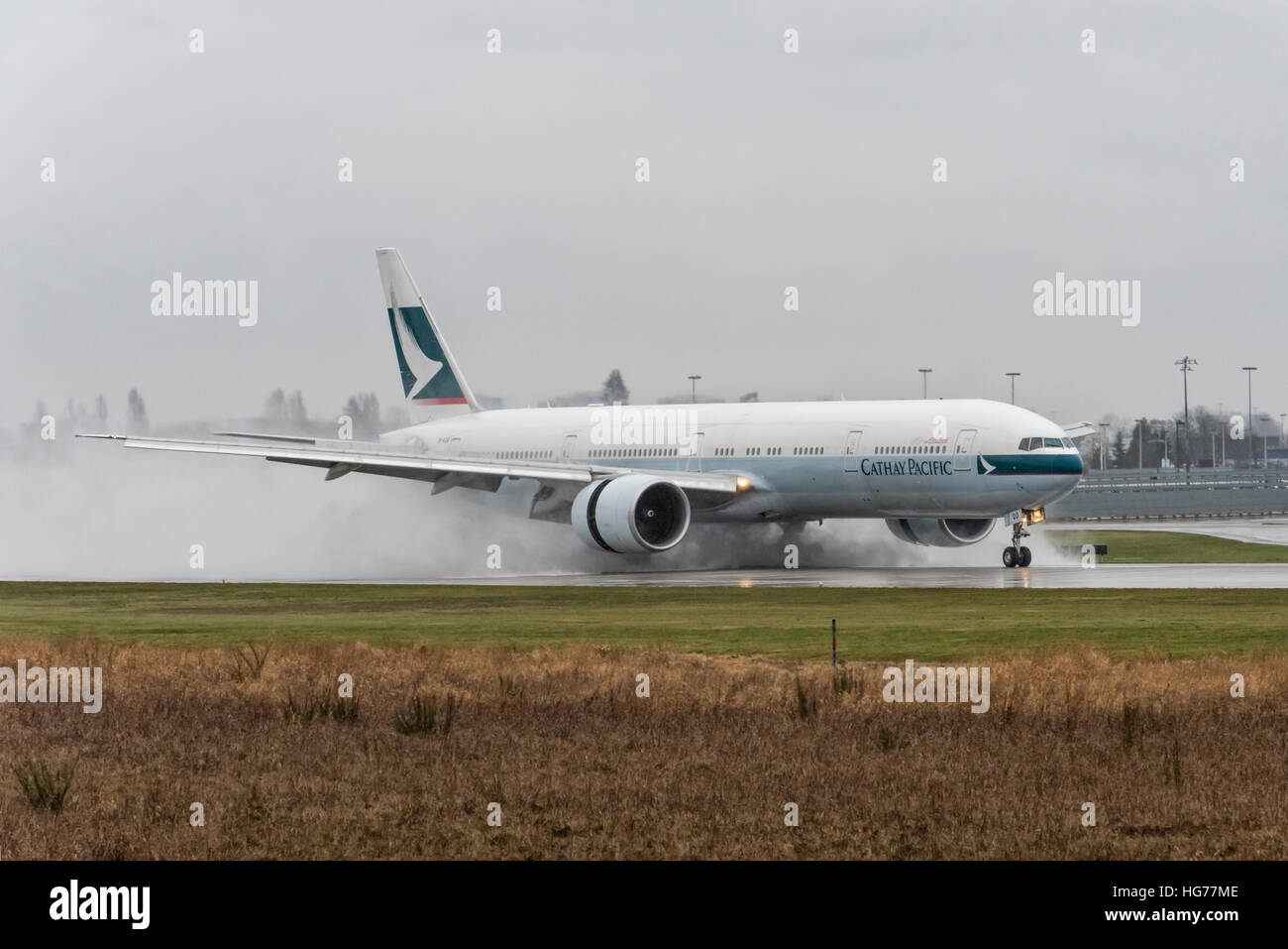 Cathay Pacific Boeing 777-300 landing on a wet runway at Vancouver International Airport. Stock Photo