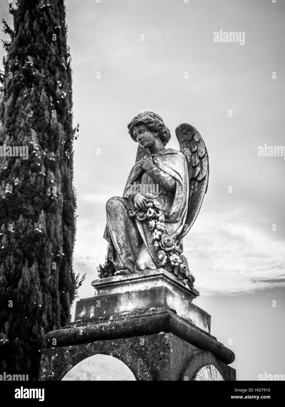A kneeling angel statue in weathered stone keeps watch over a grave beneath. Stock Photo