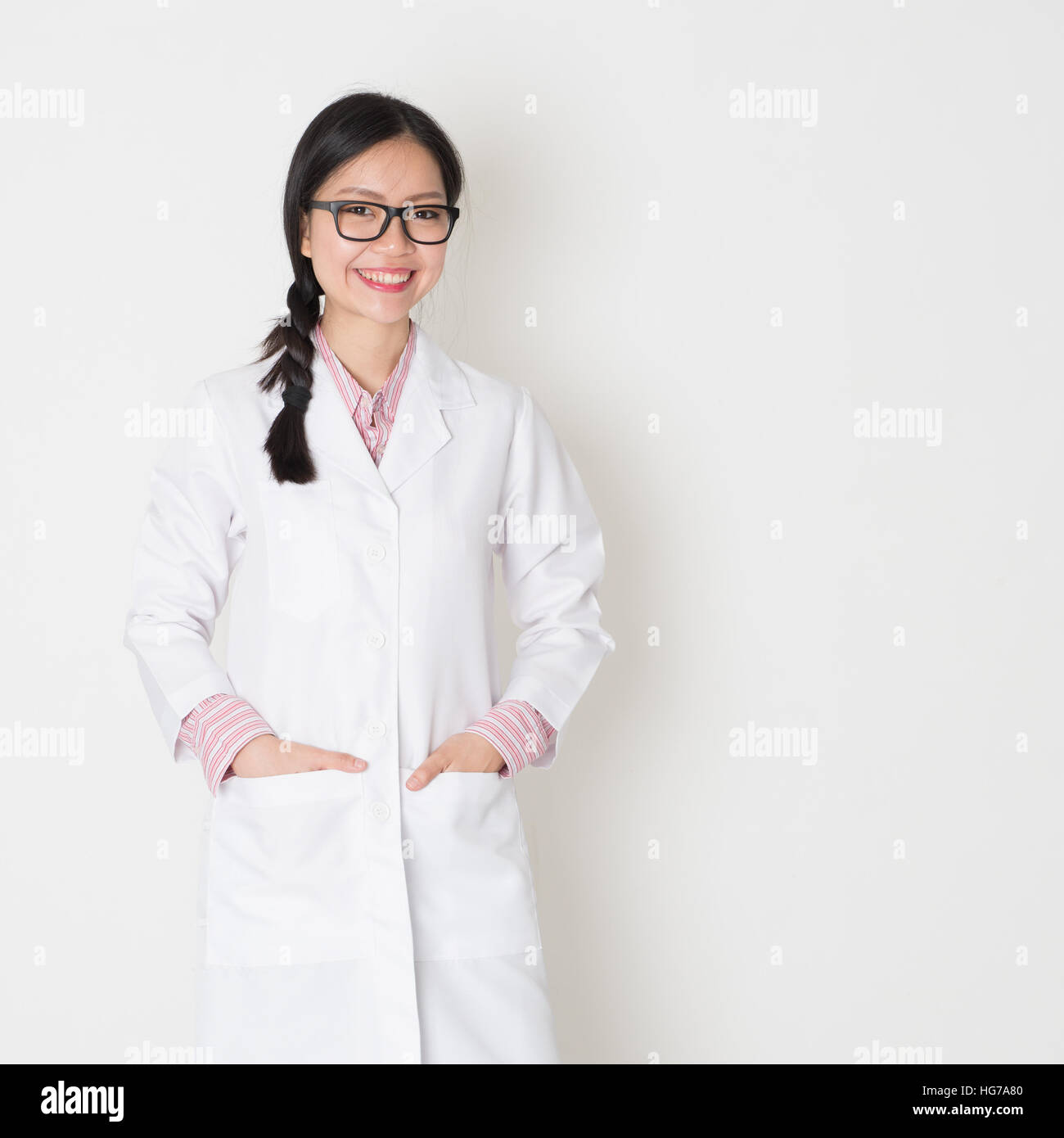 Portrait of young Asian female scientist with lab coat standing on plain background. Stock Photo