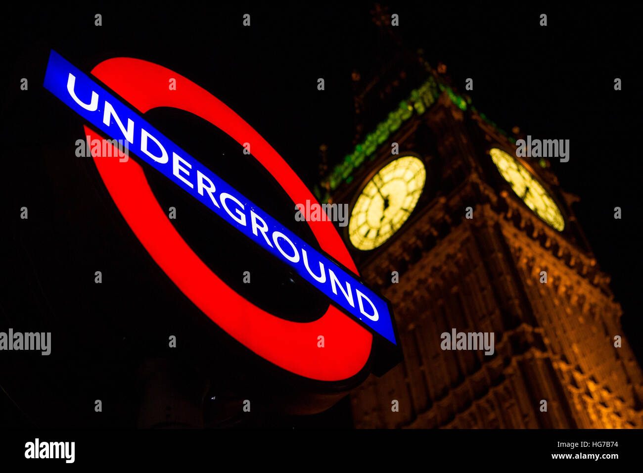 Illuminated London underground roundel tube station sign in the dark at night beside Big Ben and the palace of Westminster, Houses of Parliament Stock Photo