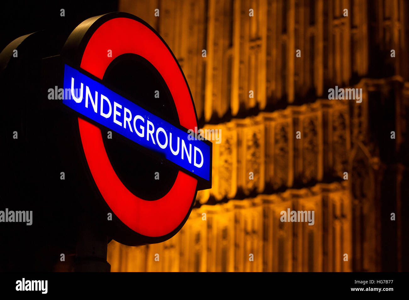 Illuminated London underground roundel tube station sign in the dark at night beside Big Ben and the palace of Westminster, Houses of Parliament Stock Photo