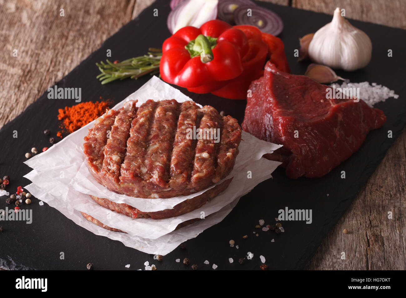 Raw Ground beef meat Burger steak cutlets with ingredients on the board. Horizontal closeup Stock Photo