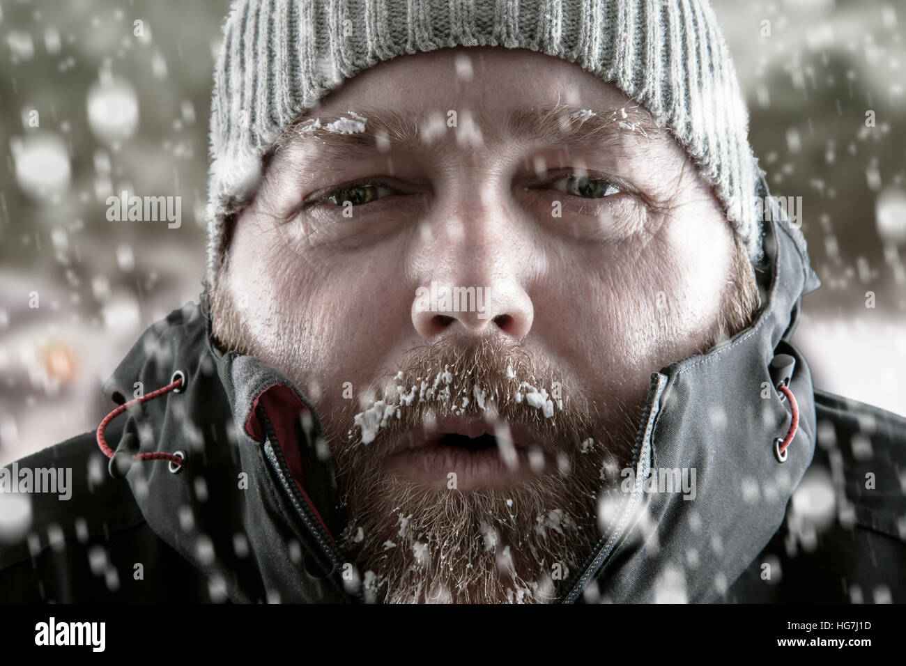 Freezing cold man portrait dressed for winter with slow falling and a snow scene background. Stock Photo
