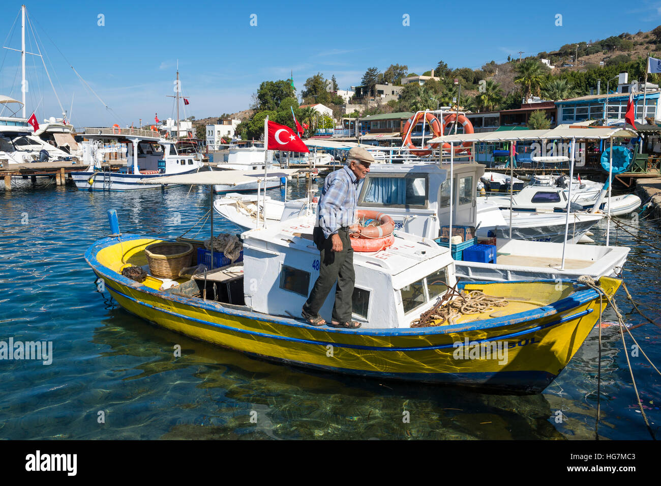 BODRUM, TURKEY - OCTOBER 10, 2016: Turkish fisherman walks along his traditional boat in the tourist town of Gumusluk. Stock Photo