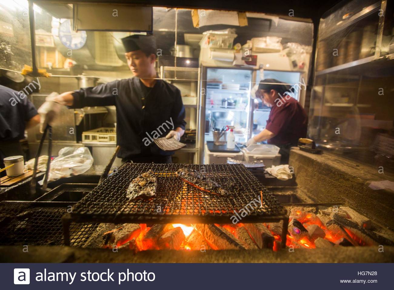 A chef standing at a charcoal grill preparing fish in a restaurant ...