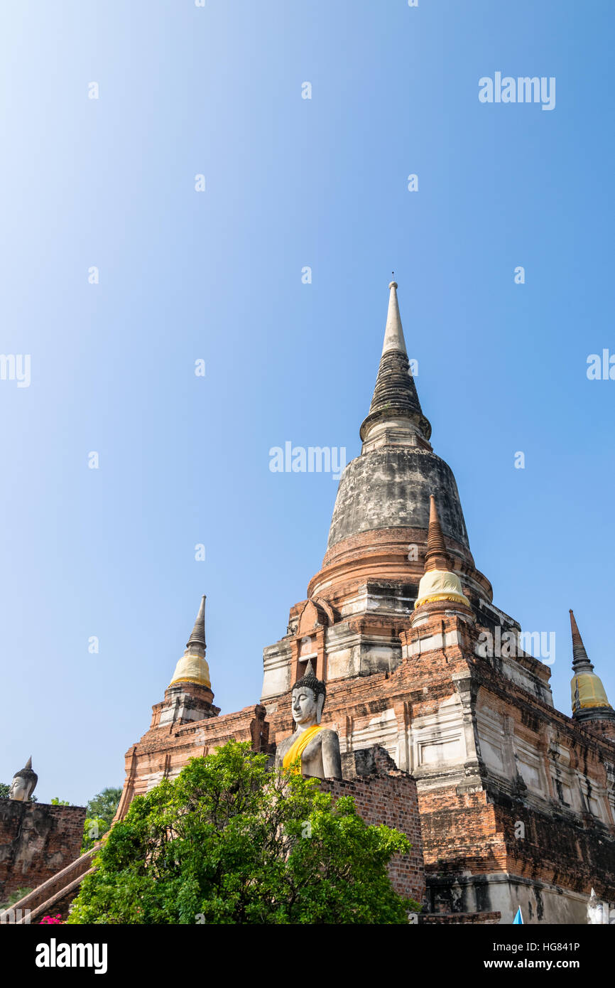 Buddha statue at the bottom of a large ancient pagoda on blue sky background at Wat Yai Chai Mongkon temple in Phra Nakhon Si Ayutthaya Historical Stock Photo