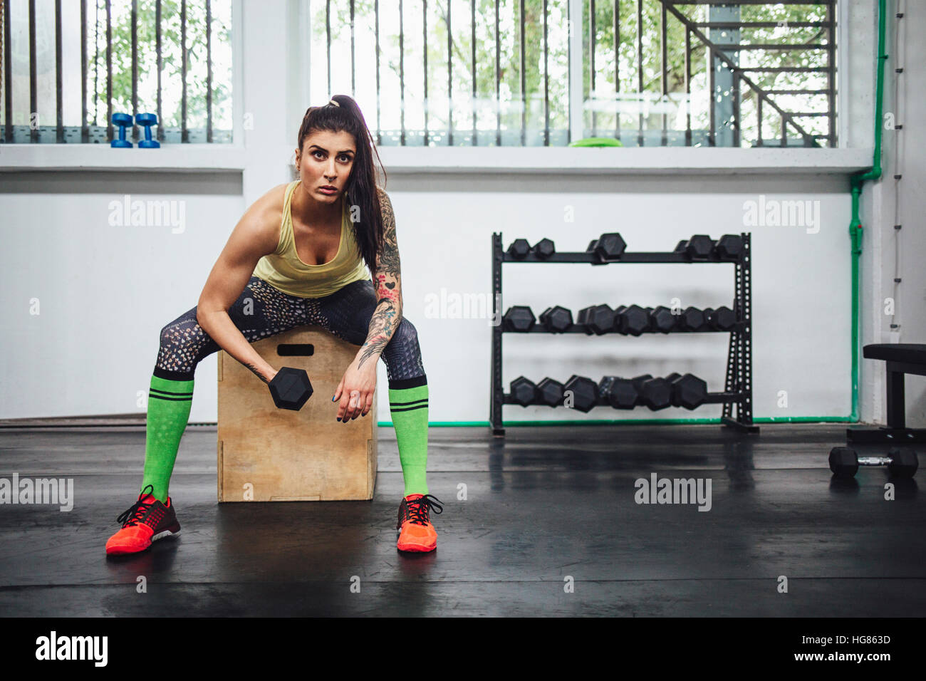 Woman lifting dumbbell while sitting on box in gym Stock Photo