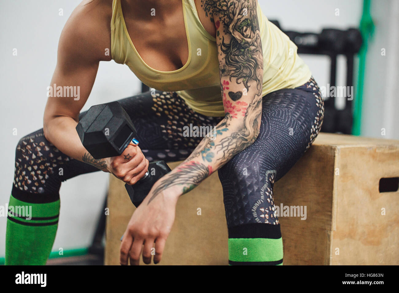 Midsection of athlete lifting dumbbell while sitting on box in gym Stock Photo
