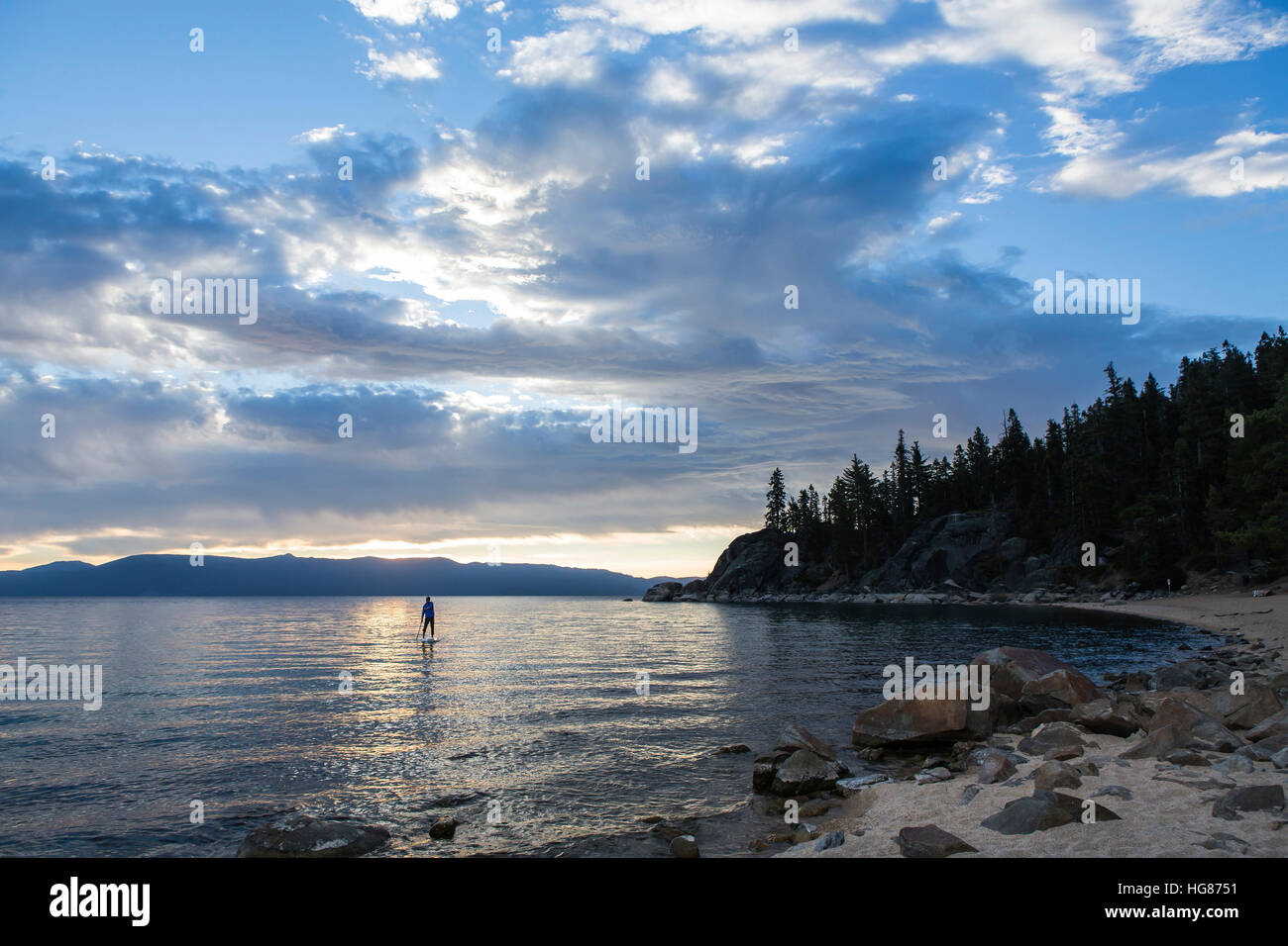 Distant view of man paddleboarding in lake against cloudy sky Stock Photo