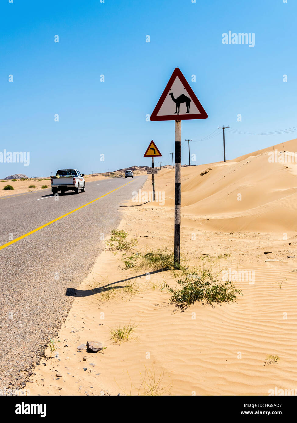 Street through sandy desert with sign warning of camel crossings, Ash Sharqiyah South, Oman Stock Photo
