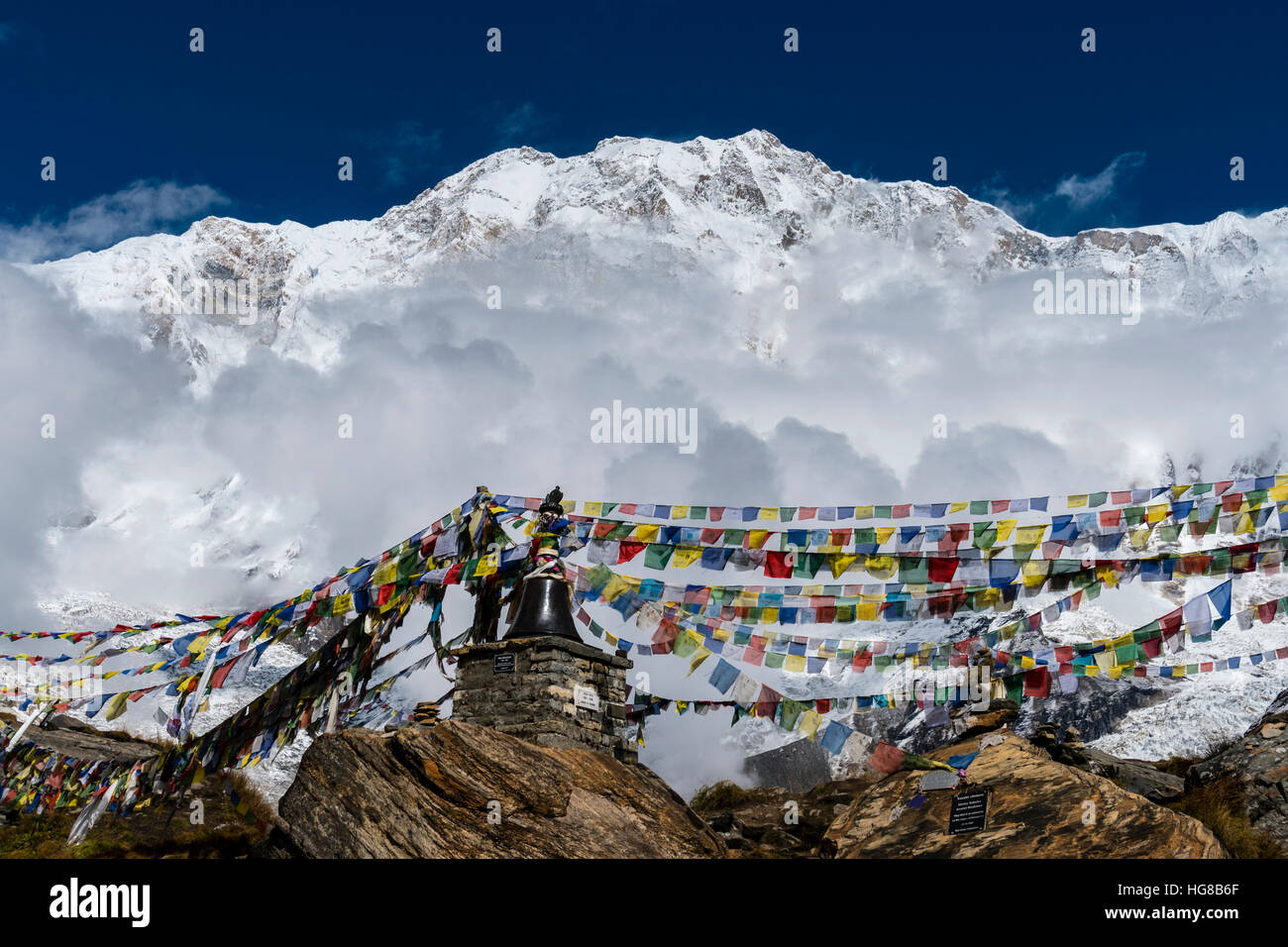 Many tibetan prayer flags are set up at a memorial for died climbers, back snow covered Annapurna 1 North Face Stock Photo
