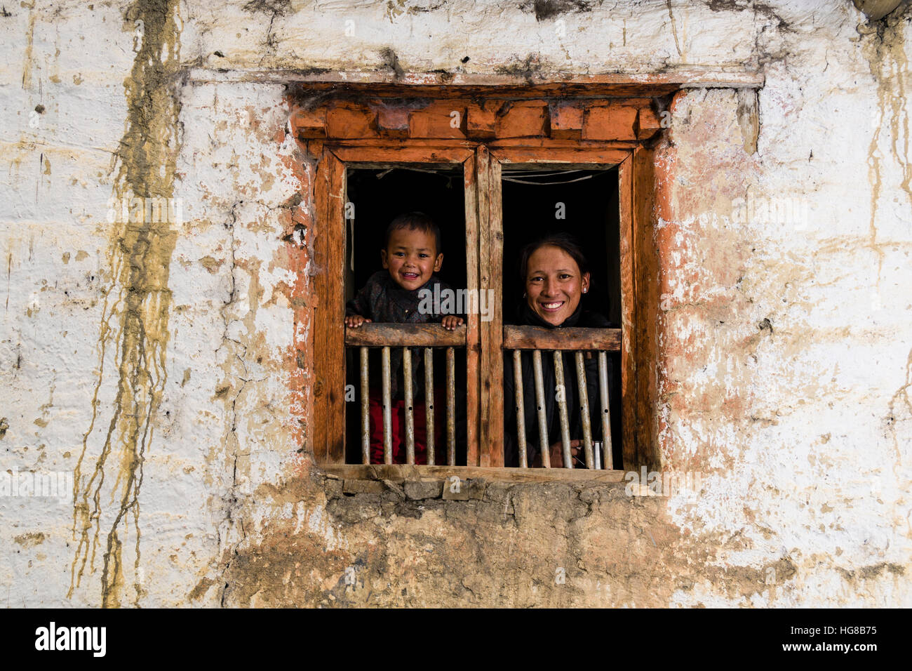Young woman and son looking out of farmhouse window, Purang, Mustang District, Nepal Stock Photo