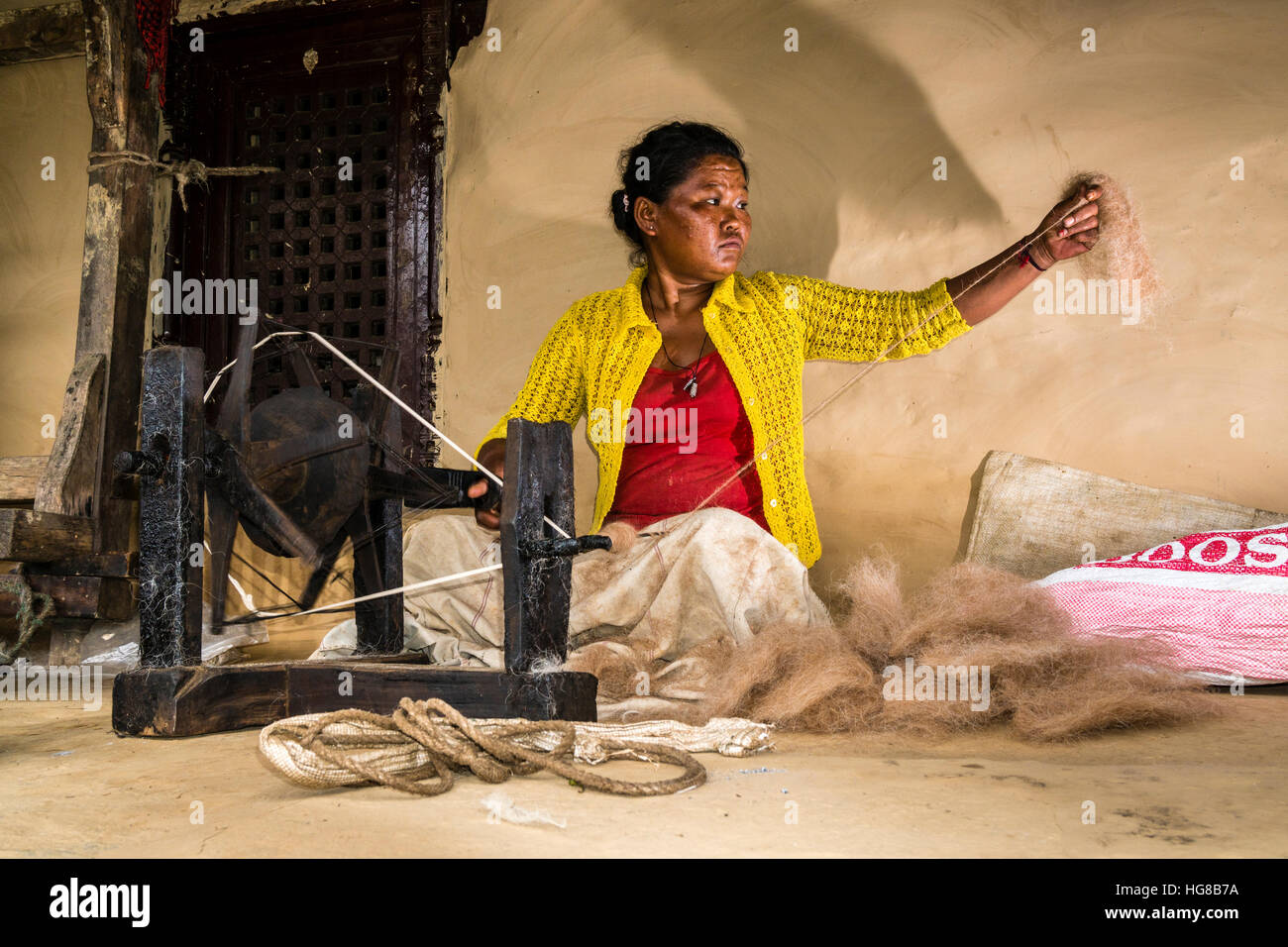 Native woman spinning sheep's wool with traditional spinning wheel in front of house, Ghandruk, Kaski District, Nepal Stock Photo